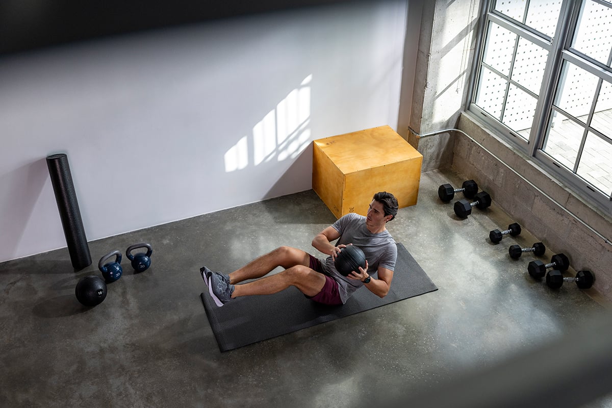 A man in a gray t-shirt does an ab workout in a gym setting.