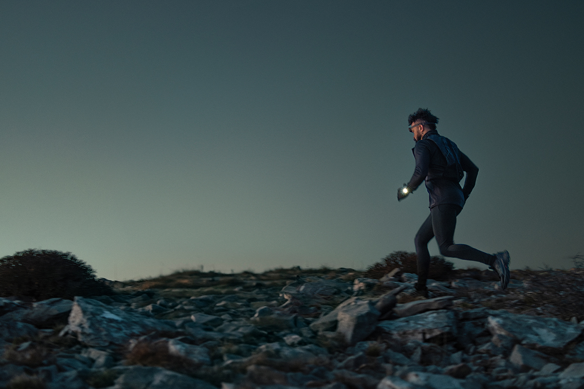 A man runs along a trail while using the flashlight on his Garmin fēnix 8 premium GPS smartwatch.