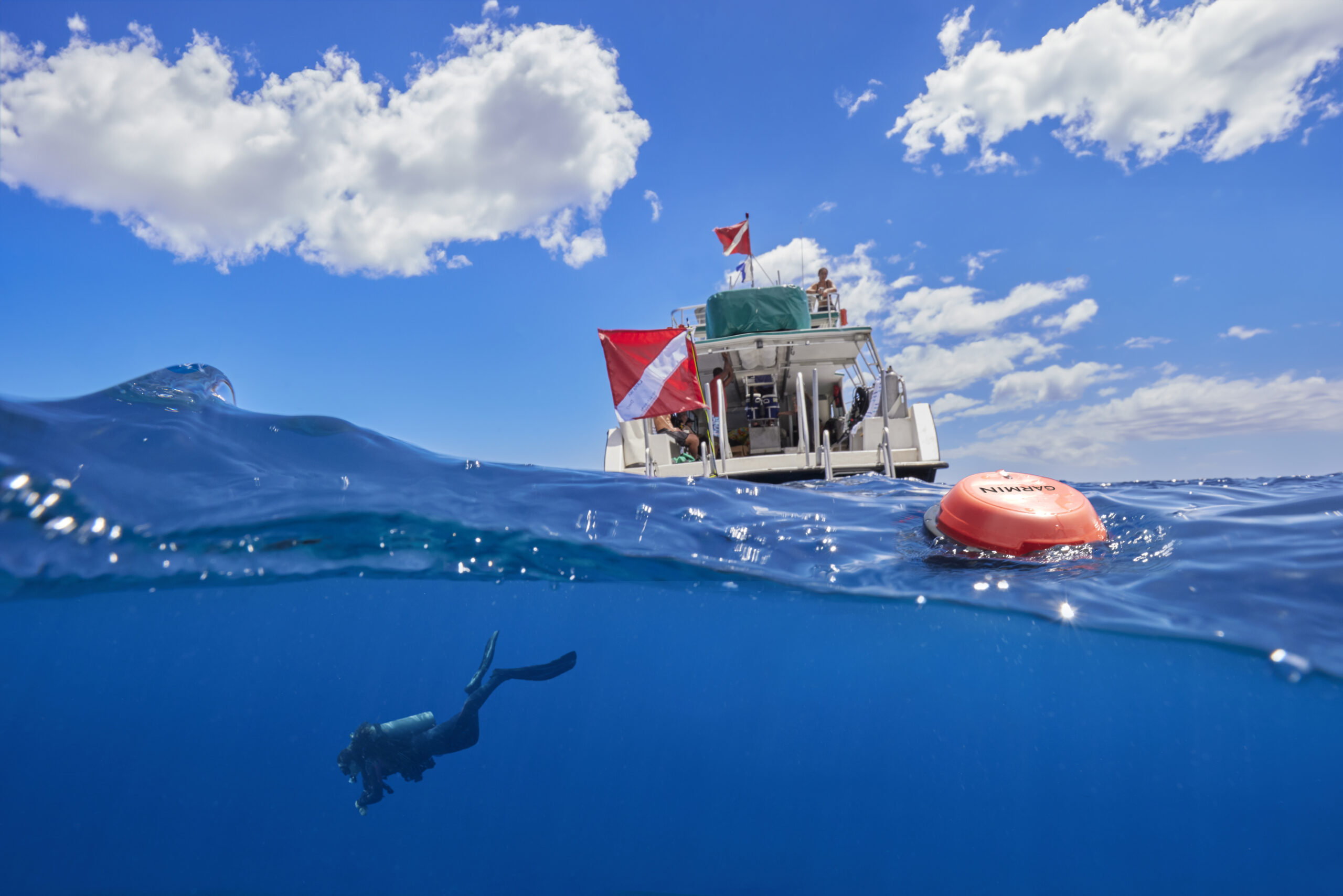The crew sits atop a boat while a diver is in the water below them. The Descent S1 Buoy floats in between the two.