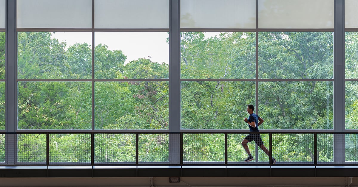 Man running across a series of windows inside a gym