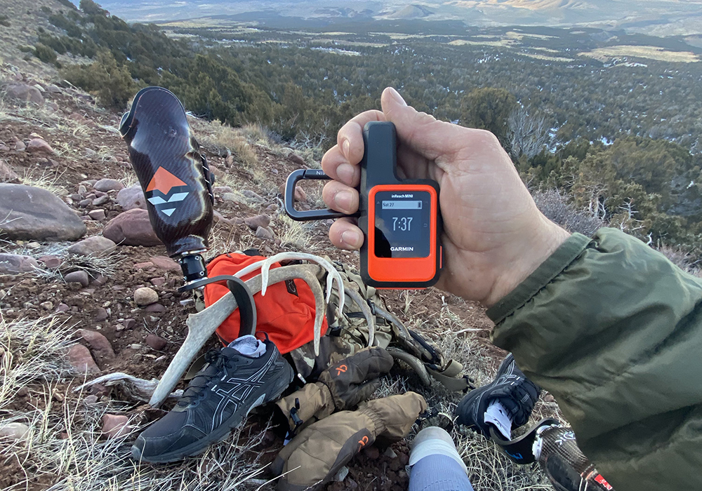 Sidney Smith holding his inReach device while sitting on a cliff.