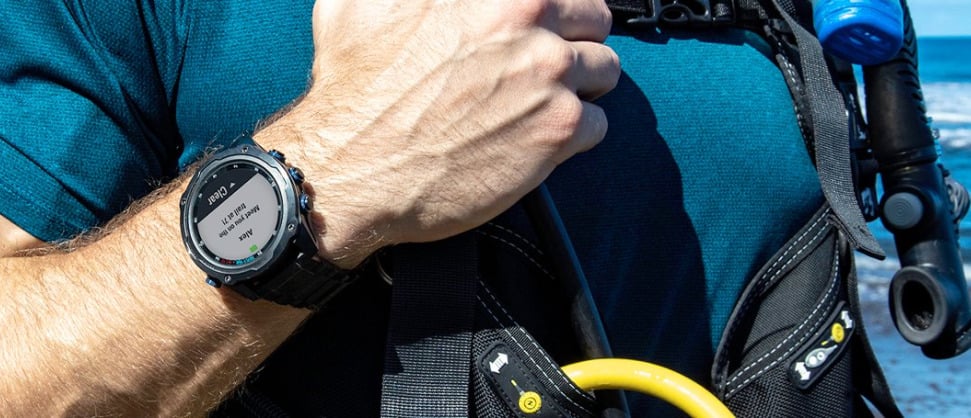 Duikcomputer van Garmin om pols bij man met duikapparatuur aan. 