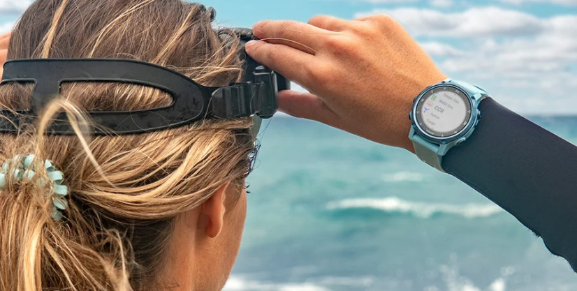 Duikcomputer Mk2S om pols van vrouw die duikbril op doet en naar de zee kijkt. 