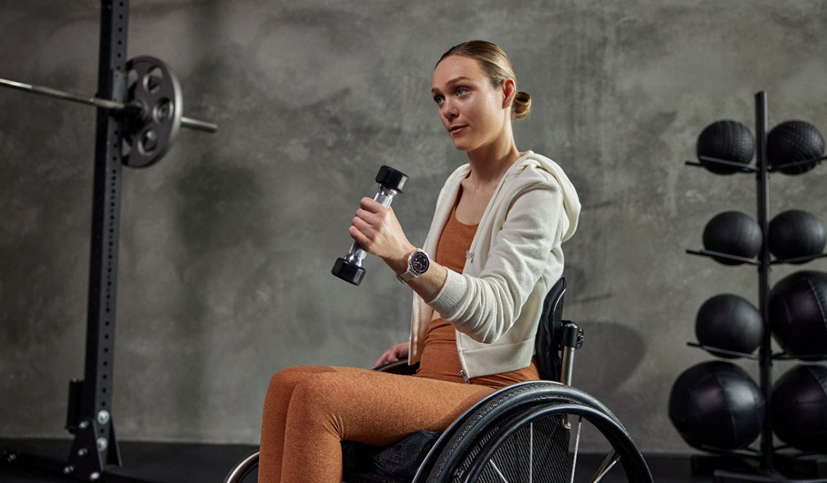 Ung kvinna i rullstol lyfter vikter med vänster arm, bär Garmin Venu 2 smartklocka.