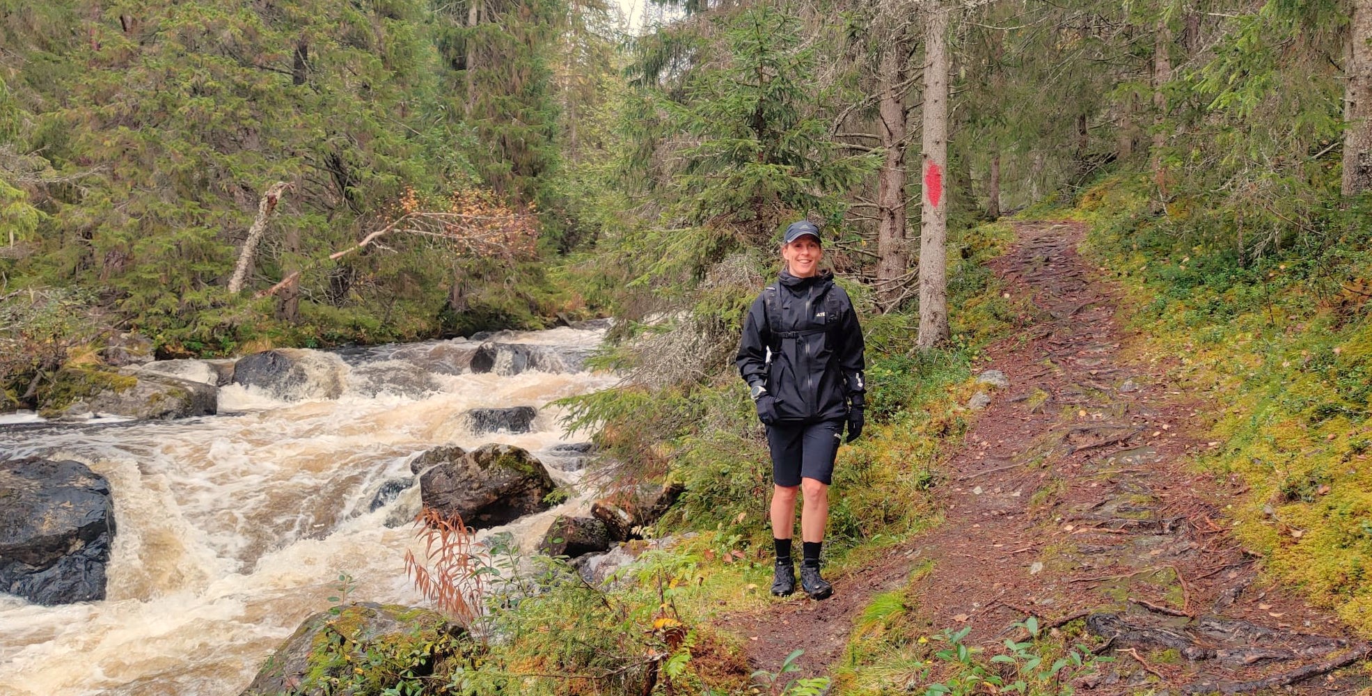 Charlotta Fougberg på en vandringsstig vid en fors i skogen.
