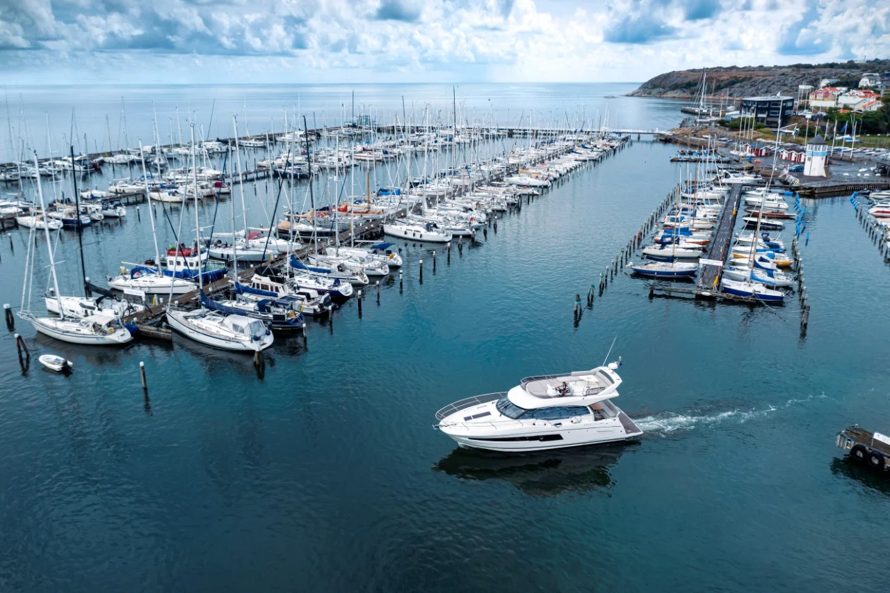 Motorbåt lämnar marina med segelbåtar och bryggor i bakgrunden